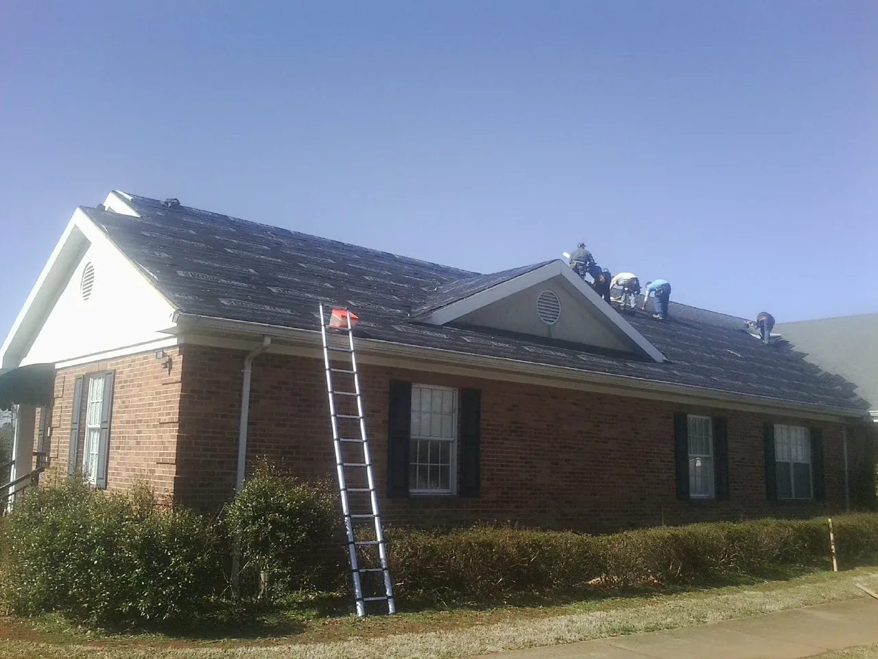 Crew tearing shingles off a brick ranch roof with a ladder set — Metal Roof Repair work by our crew in Long Grove