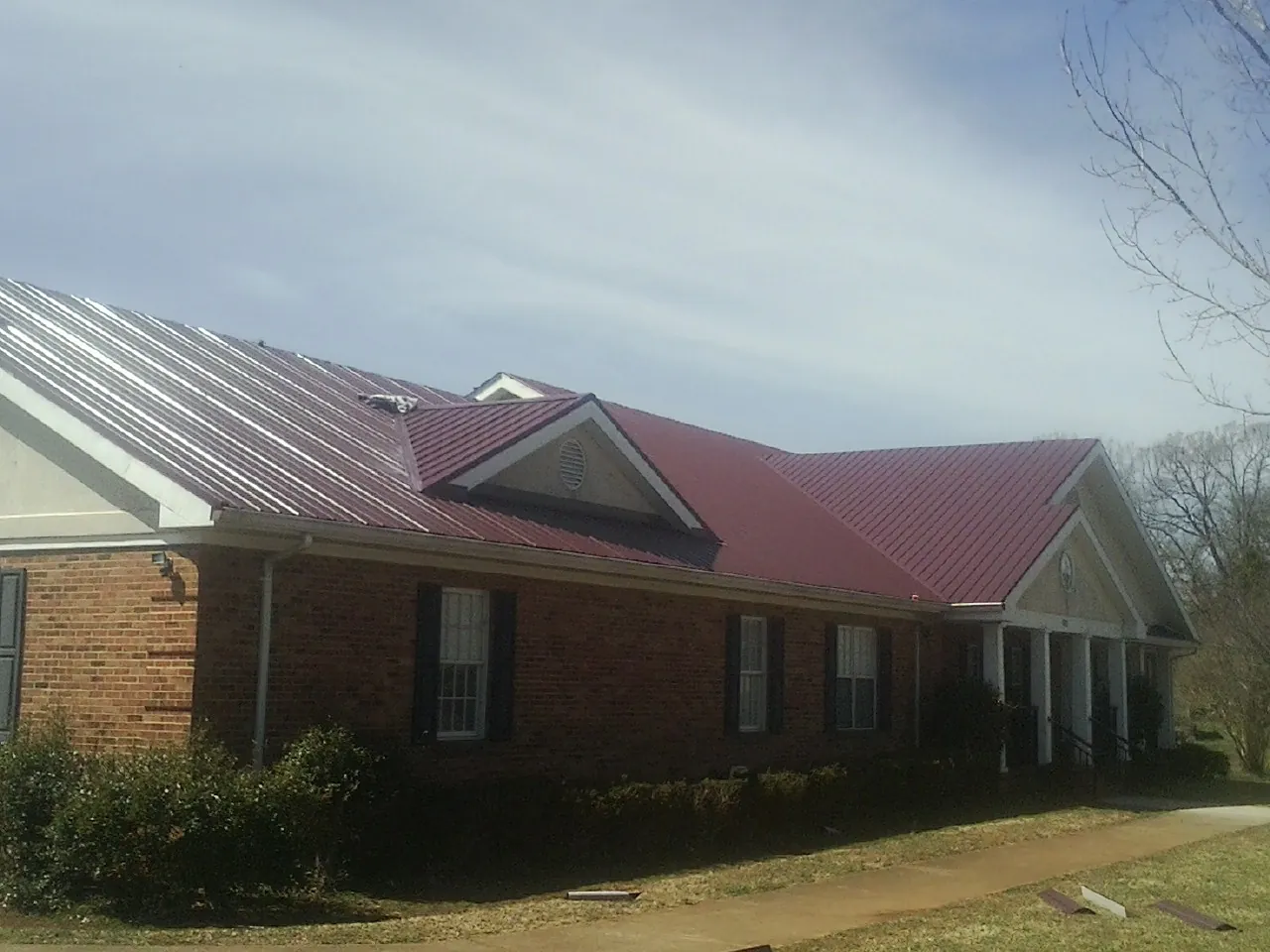 Red metal roof with gabled entries on a long brick building, from a Hail Damage Roof Repair job in Long Grove