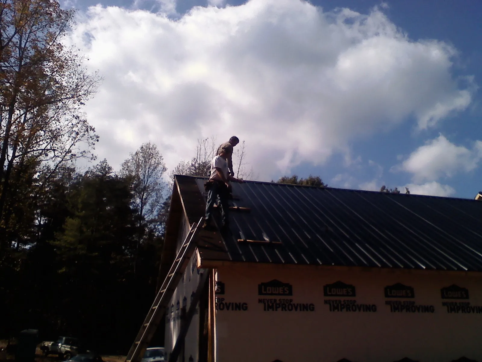 Roofer fastening dark metal panels high against a cloudy sky, from a Roof Inspection job in Long Grove