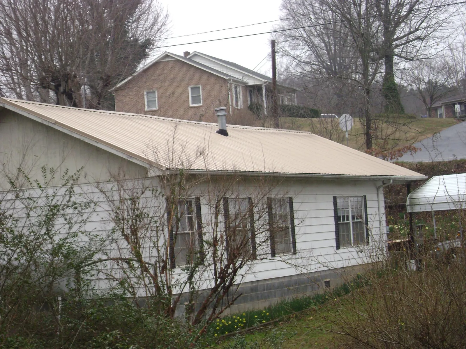 Tan metal roof on a white sided house set into a hillside — Commercial Roofing by Roofing Brothers in Long Grove